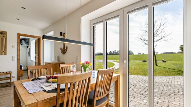 Un comedor moderno con una mesa de madera, sillas y vistas a un paisaje verde a través de amplios ventanales.