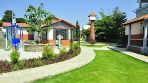 A well-maintained courtyard with a playground, a small building with a sign, and a tall structure with a pointed roof. - Nirvana Club Resort and Spa (Anekal)