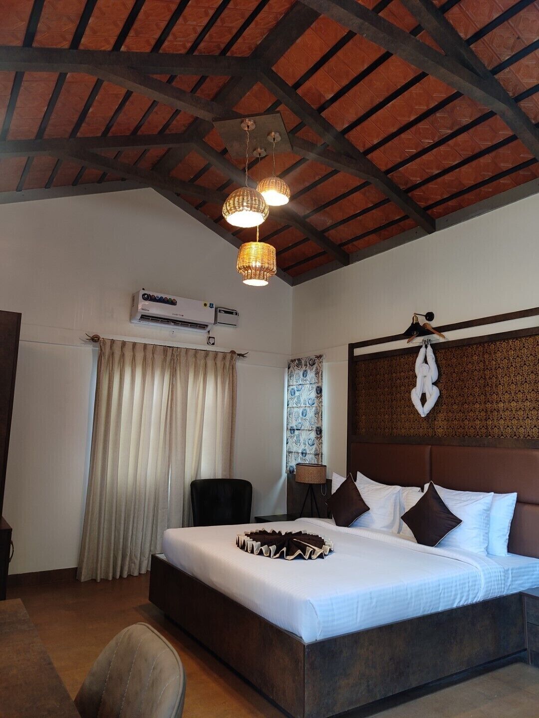A hotel room with a large bed, a ceiling fan, an air conditioning unit, and a decorative wall hanging.