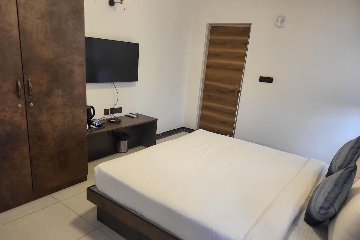 Quarto de hotel com cama, escrivaninha, televisão de tela plana, guarda-roupa e lixeira.