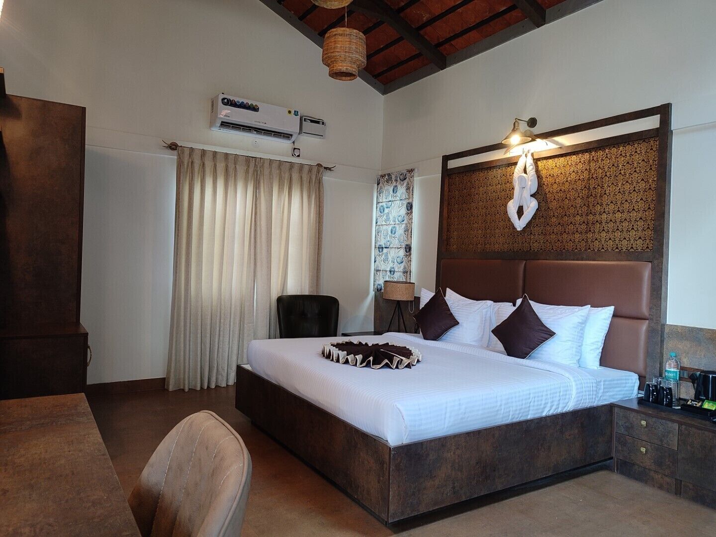 A hotel room with a large bed, a desk, a chair, an air conditioning unit, and a decorative wall panel.
