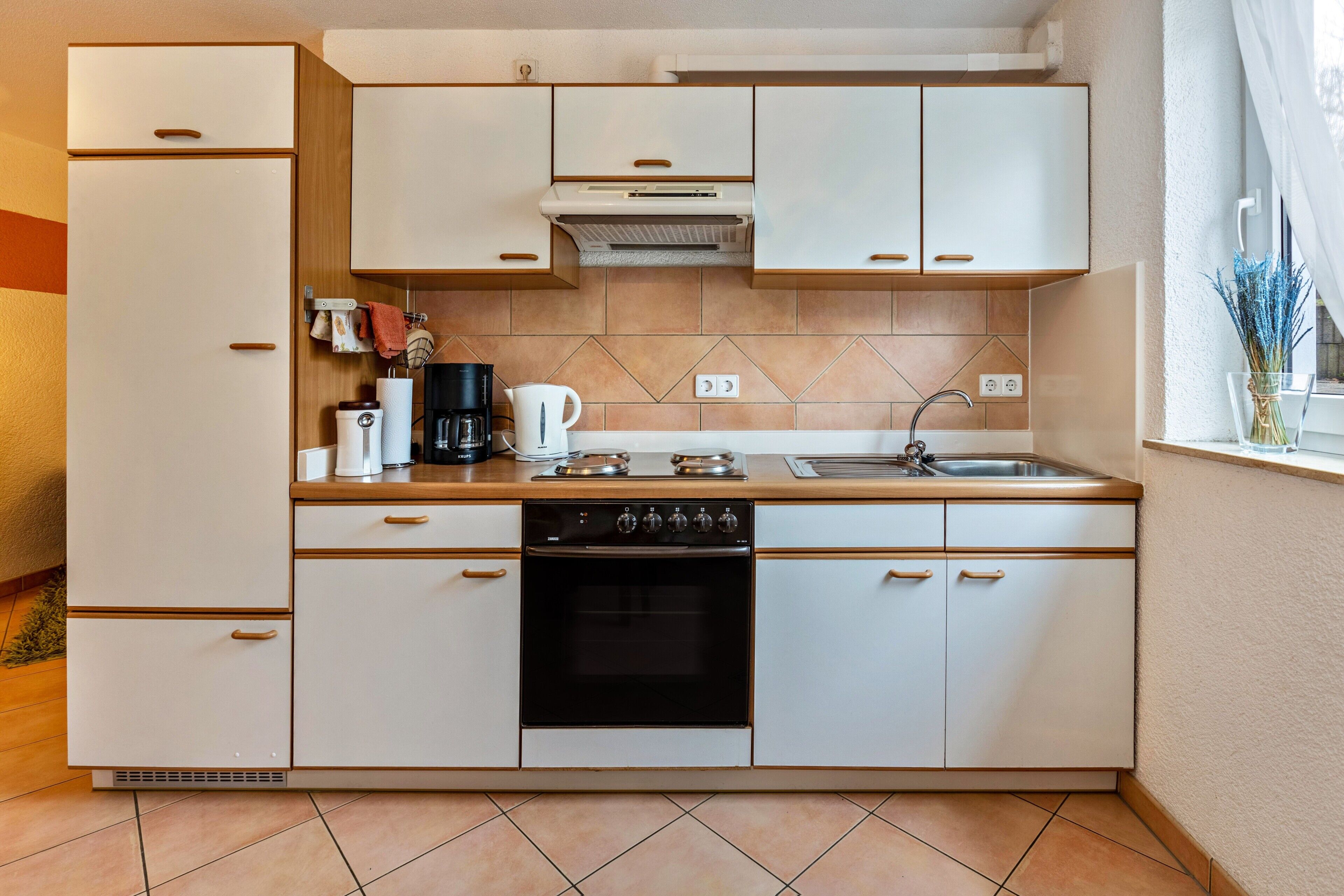 A compact kitchen with white cabinetry, a built-in oven, a coffee maker, and a window with a view.