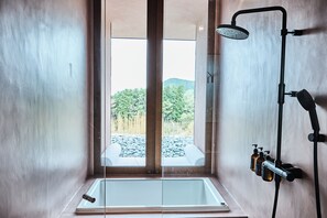 Ein modernes Badezimmer mit einer gläsernen Badewanne, einer Handbrause und zwei Shampoo-Flaschen.