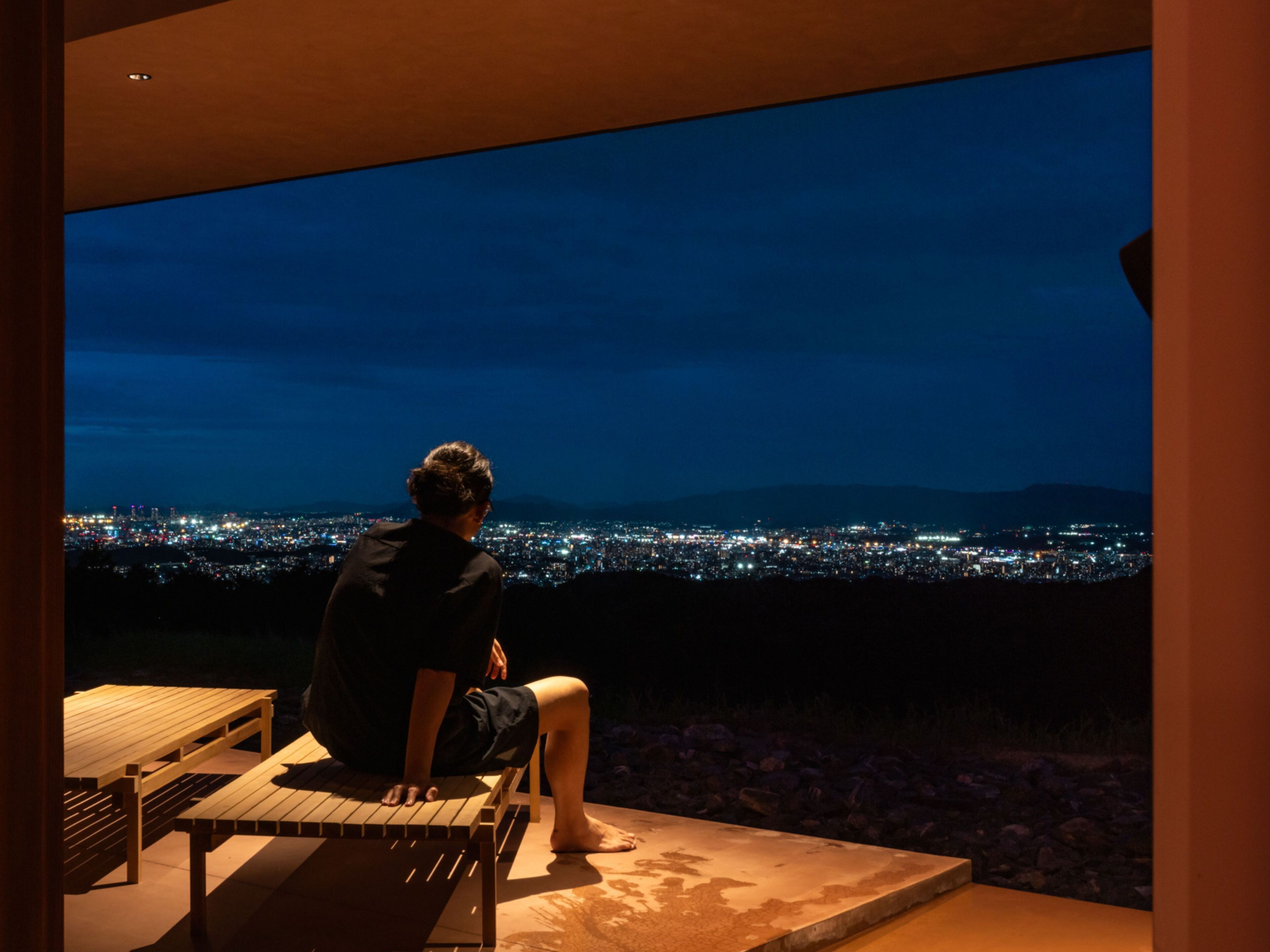Uma pessoa sentada num banco admirando uma vista noturna da cidade.