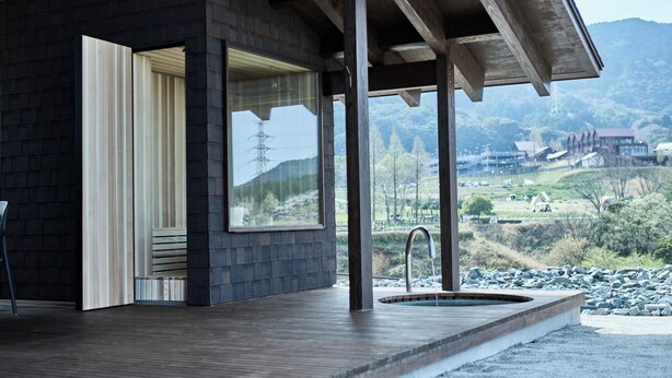 Un edificio moderno con terraza de madera, un ventanal grande y vistas a un paisaje montañoso.