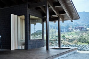 A modern building with a wooden deck, a large window, and a view of a mountainous landscape. - Snow Peak YAKEI SUITE ABURAYAMA FUKUOKA (Fukuoka)