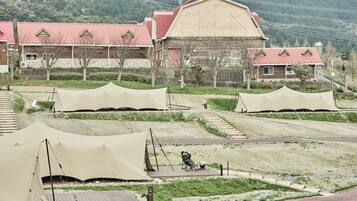 A campsite with tents, a wooden deck, and a large building with a red roof.