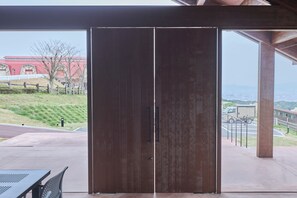 A large wooden door with a metal handle, leading to an outdoor area with a view of a building and a hilly landscape. - Snow Peak YAKEI SUITE ABURAYAMA FUKUOKA (Fukuoka)
