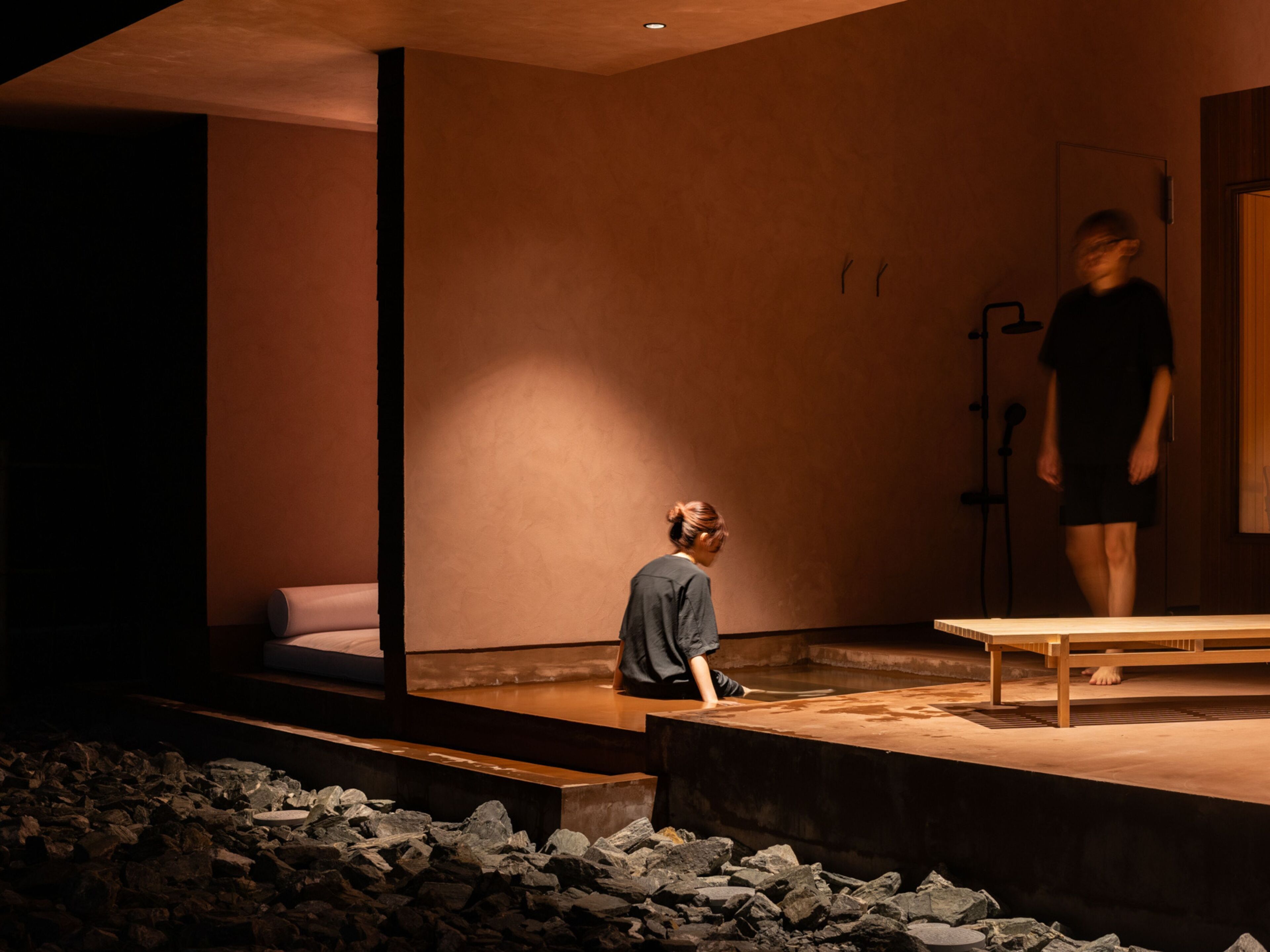 A modern interior with a stone floor, a wooden bench, and a person sitting on a platform.