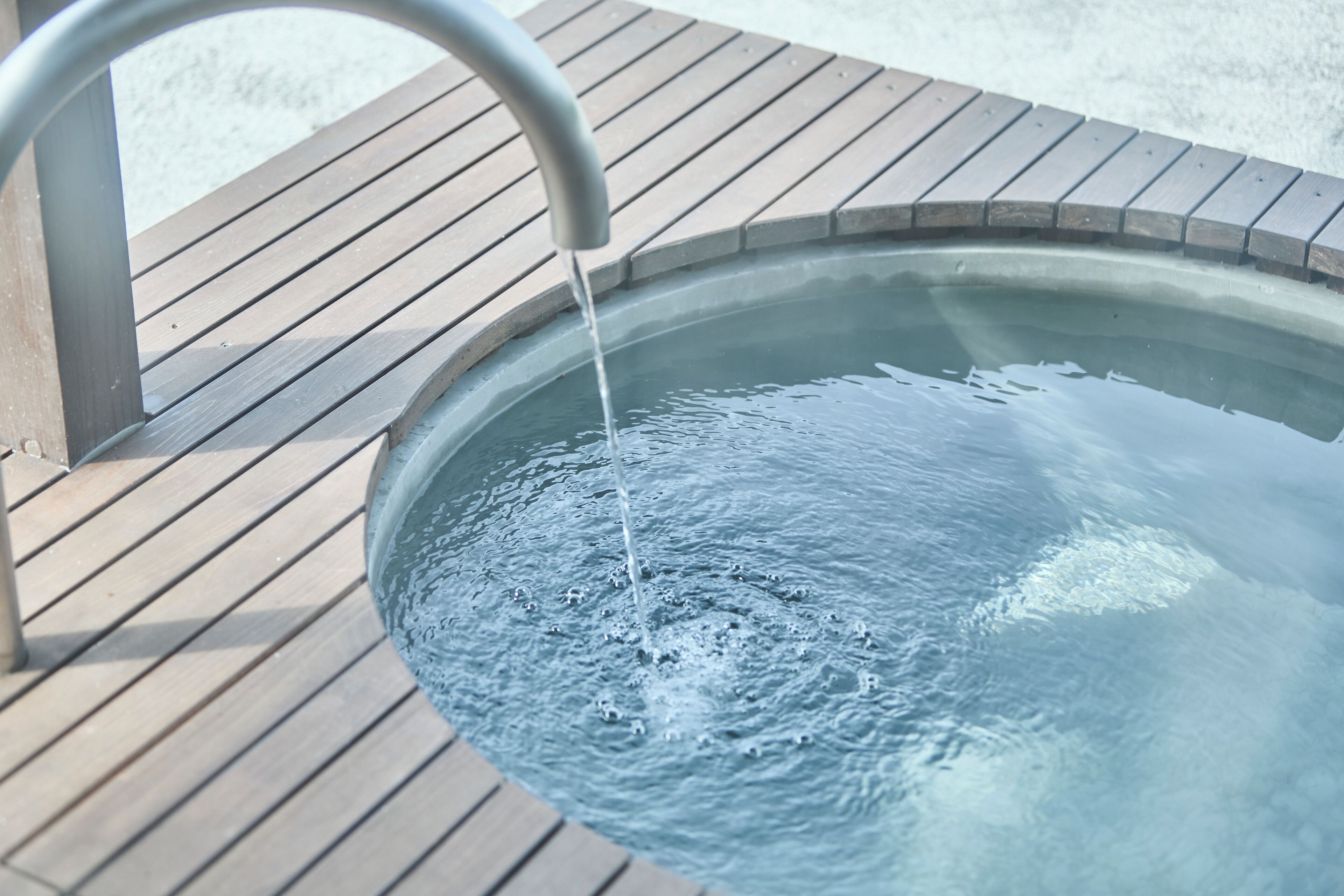 A hot tub with water flowing from a faucet, surrounded by a wooden deck.