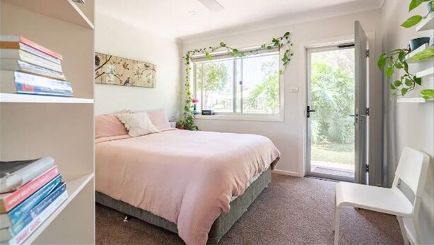Makuuhuone, jossa on sänky, kattotuuletin, ikkuna, josta on näkymä, kirjahylly ja tuoli.