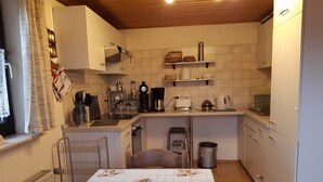 Una cucina compatta con elettrodomestici essenziali, un tavolo da pranzo con tovaglia a fiori e un piccolo sgabello.