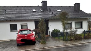 Un edificio residenziale con tetto in tegole, un'auto rossa parcheggiata nel vialetto e il numero '12' sulla facciata.