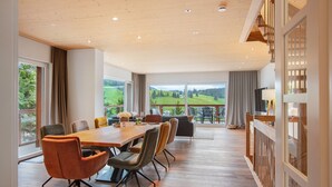 Habitación amplia con una mesa de madera para comer, varias sillas, un sofá y un ventanal que ofrece vistas a un paisaje verde.