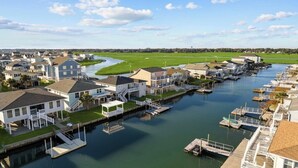A marina with houses docked along the water, a grassy field in the background, and a clear sky. - 5BR Waterfront w/ Heated Pool | Fire Pit | Grill (North Myrtle Beach)