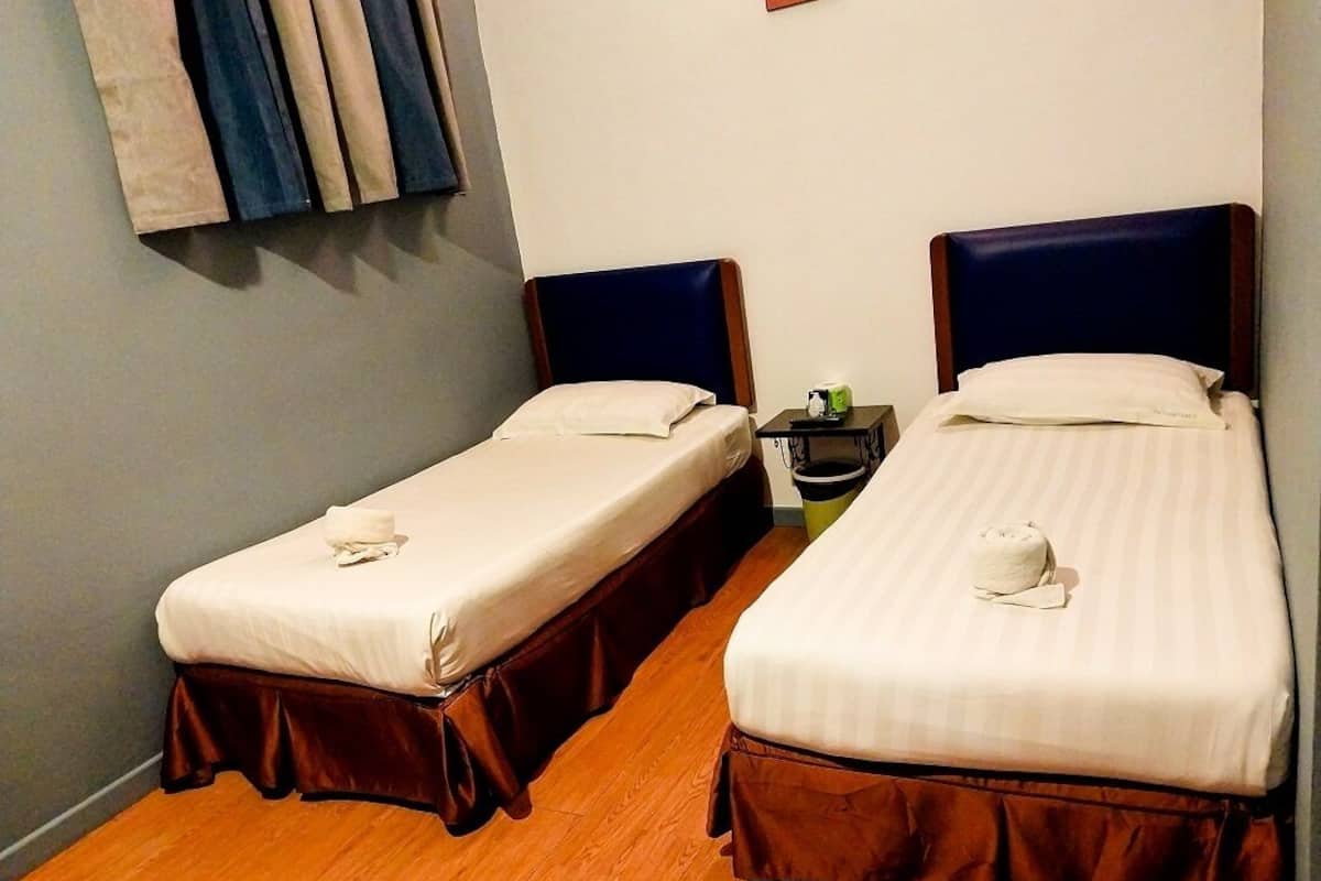 Dos camas individuales con cabeceros de madera y falda combinada, una mesita con un objeto verde y una cortina fijada a la pared.