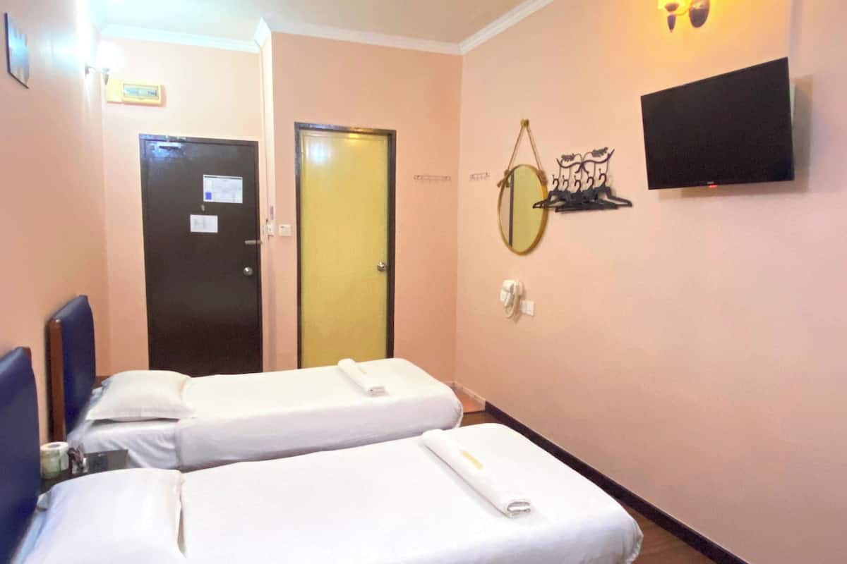 Habitación de hotel con dos camas individuales, un televisor de pantalla plana montado en la pared y una puerta con un cartel encima.