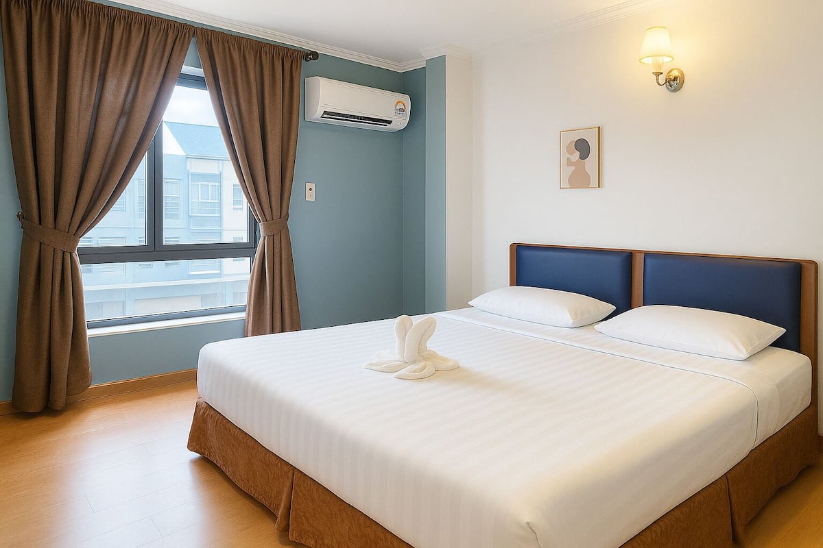 Habitación de hotel con cama, cortinas, aire acondicionado, una lámpara de pared y ventana con vistas a edificios.
