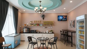 Una cocina moderna con comedor, refrigerador, microondas, cafetera y televisor en la pared.