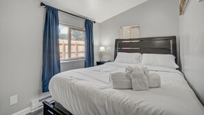 Ein ordentlich bezogenes Bett mit weißen Leinen und Handtüchern, ein Nachttisch mit Lampe und ein Fenster mit blauen Vorhängen.