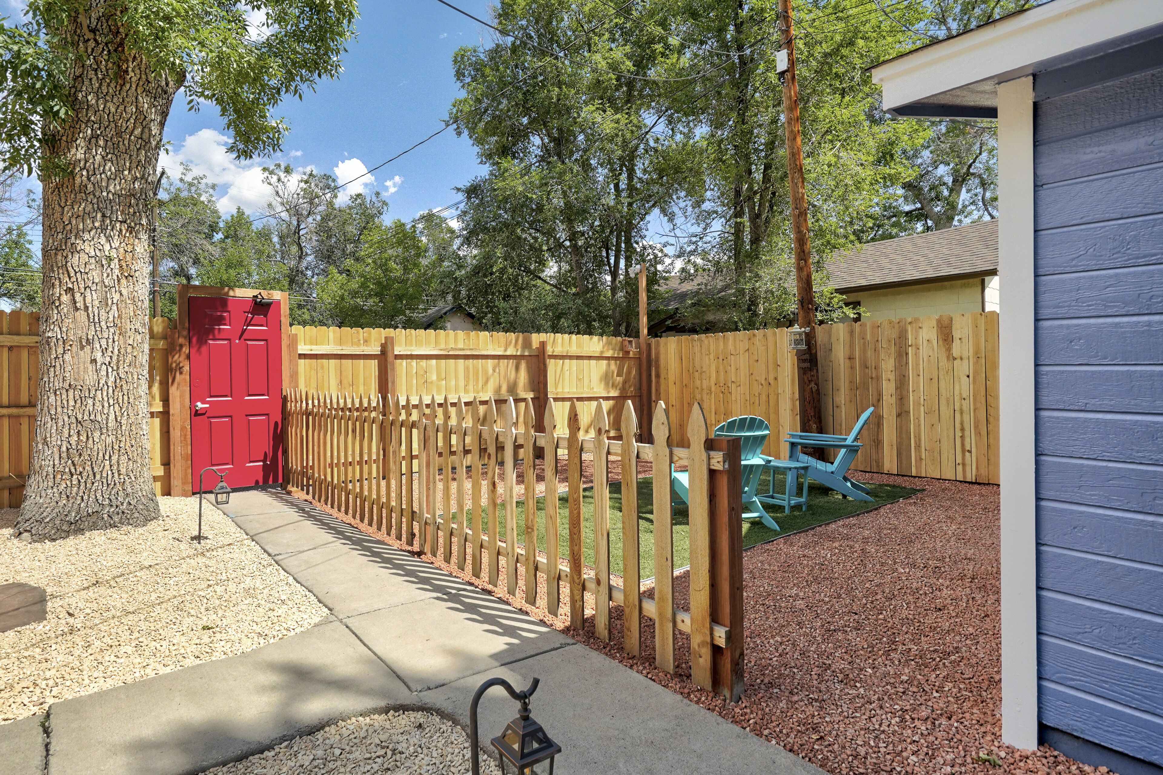A fenced backyard with a red door, a wooden fence, a blue chair, and a shed.