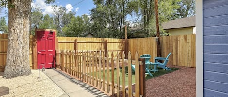 A fenced backyard with a red door, a wooden fence, a blue chair, and a shed.