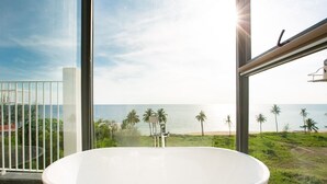 A modern bathroom with a freestanding bathtub, large windows, and a view of the beach and ocean.
