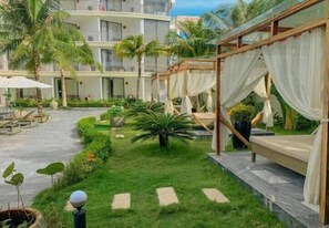 A courtyard with a grassy area, palm trees, and a covered seating area with white curtains. - The Palmy Luxury Beach Phu Quoc (Phu Quoc)