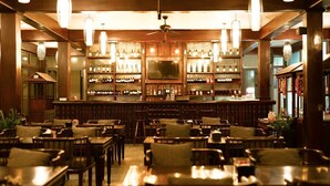 A bar area with wooden furniture, shelves of bottles, and hanging lights.