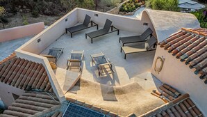 An outdoor patio area with multiple lounge chairs and a small table, surrounded by a low wall and a tiled roof. - Villa Anga 10 1 Emma Villas (Arzachena)