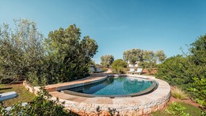A circular pool with a stone border, surrounded by lush greenery and trees. - Borgo Dell Agrumeto 8 Emma Villas (Ostuni)