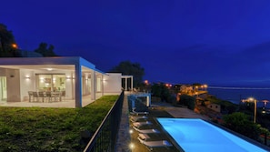 A modern house with a swimming pool, outdoor seating, and a view of the sea at dusk. - Villa Gioia 8 Emma Villas (Sanremo)