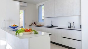 A modern kitchen with white cabinetry, a black countertop, and a bowl of fresh vegetables. - Villa Gioia 8 Emma Villas (Sanremo)
