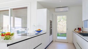 A modern kitchen with white cabinetry, a large window, and a bowl of fruit on the counter. - Villa Gioia 8 Emma Villas (Sanremo)