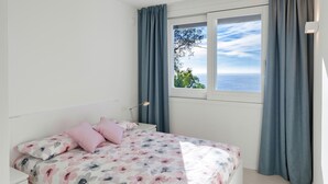 A bedroom with a bed, a nightstand, a lamp, and a window with a view of the sea. - Villa Gioia 8 Emma Villas (Sanremo)