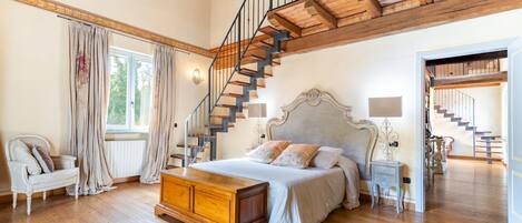 A spacious bedroom with a large bed, a wooden staircase, and a view of the outdoors.