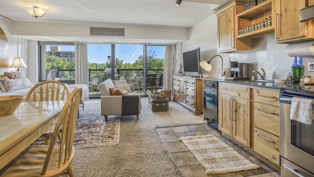 A modern kitchen with wooden cabinets, a dining area with a table and chairs, and a large sliding glass door leading to a balcony.