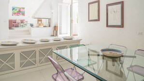A bright, modern kitchen with a glass dining table, white cabinetry, and a view to the living area. - Villa Borboleta By Elite Villas (Capri)