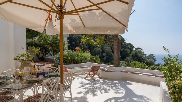 A terrace with outdoor furniture, a table set for dining, and a view of the sea. - Villa Borboleta By Elite Villas (Capri)