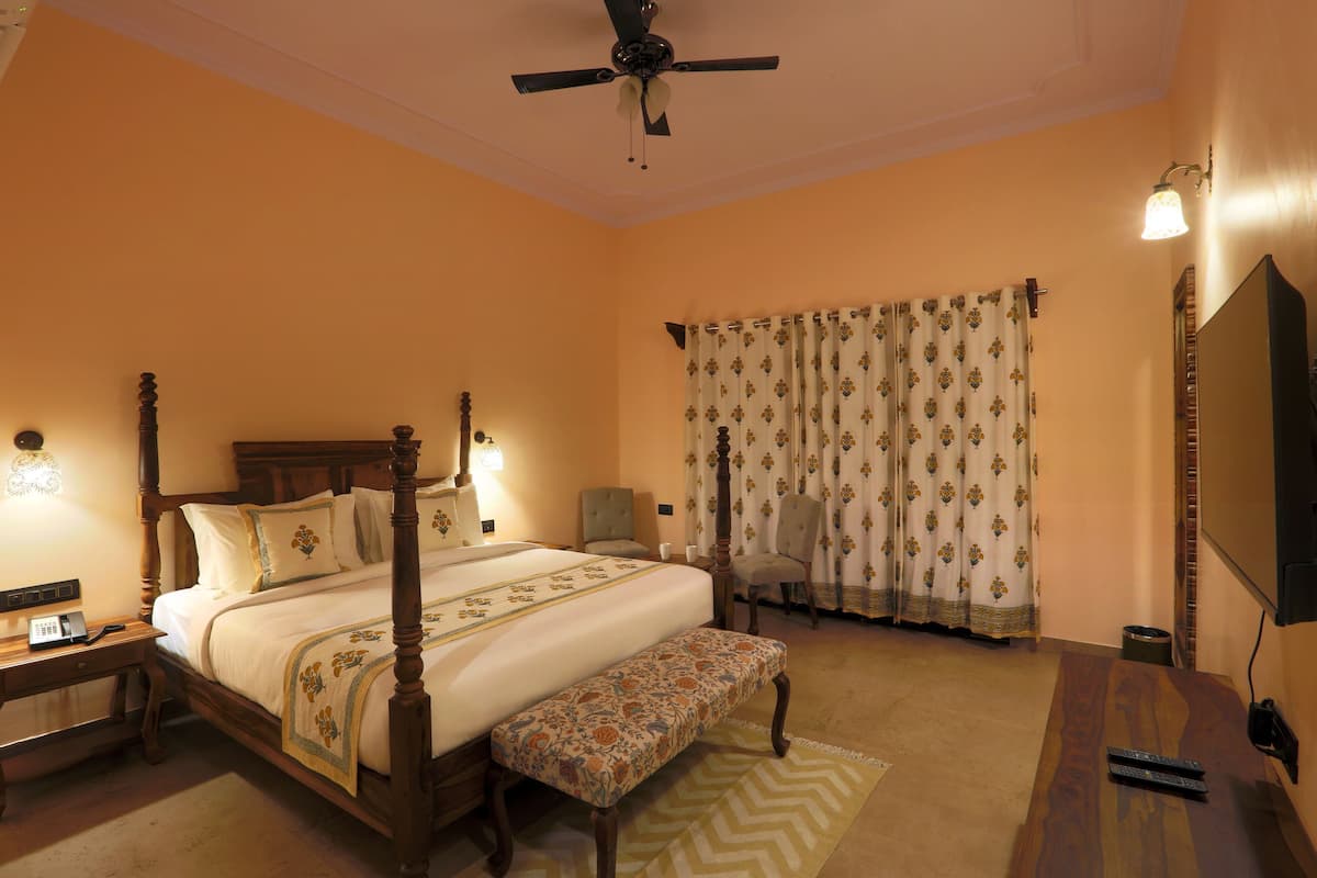 A four-poster bed with a bench, a desk with a telephone, a chair, and a television on the wall.