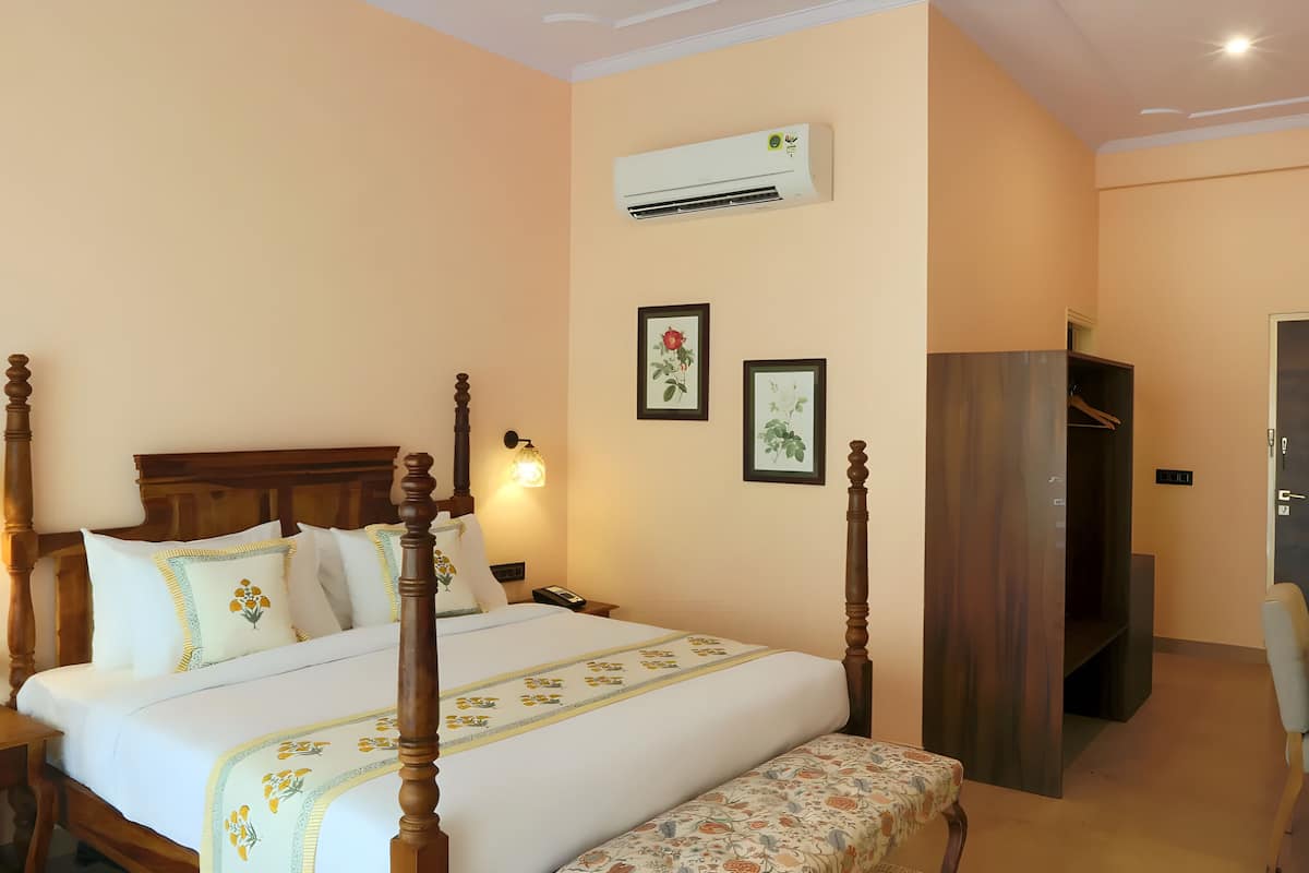 A neatly arranged hotel room with a four-poster bed, bedside tables, a bench, and a wardrobe.