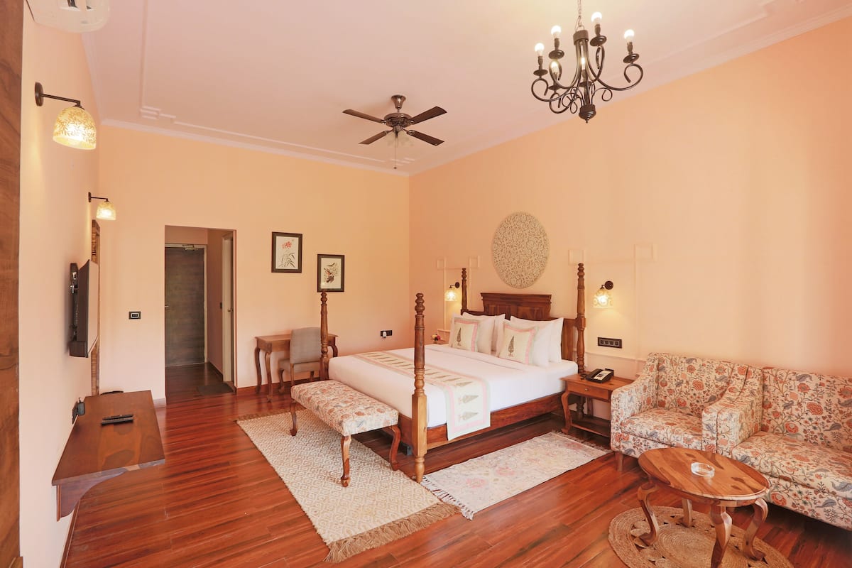 A bedroom with a four-poster bed, a wooden bench, a sofa, a small table, and a ceiling fan.