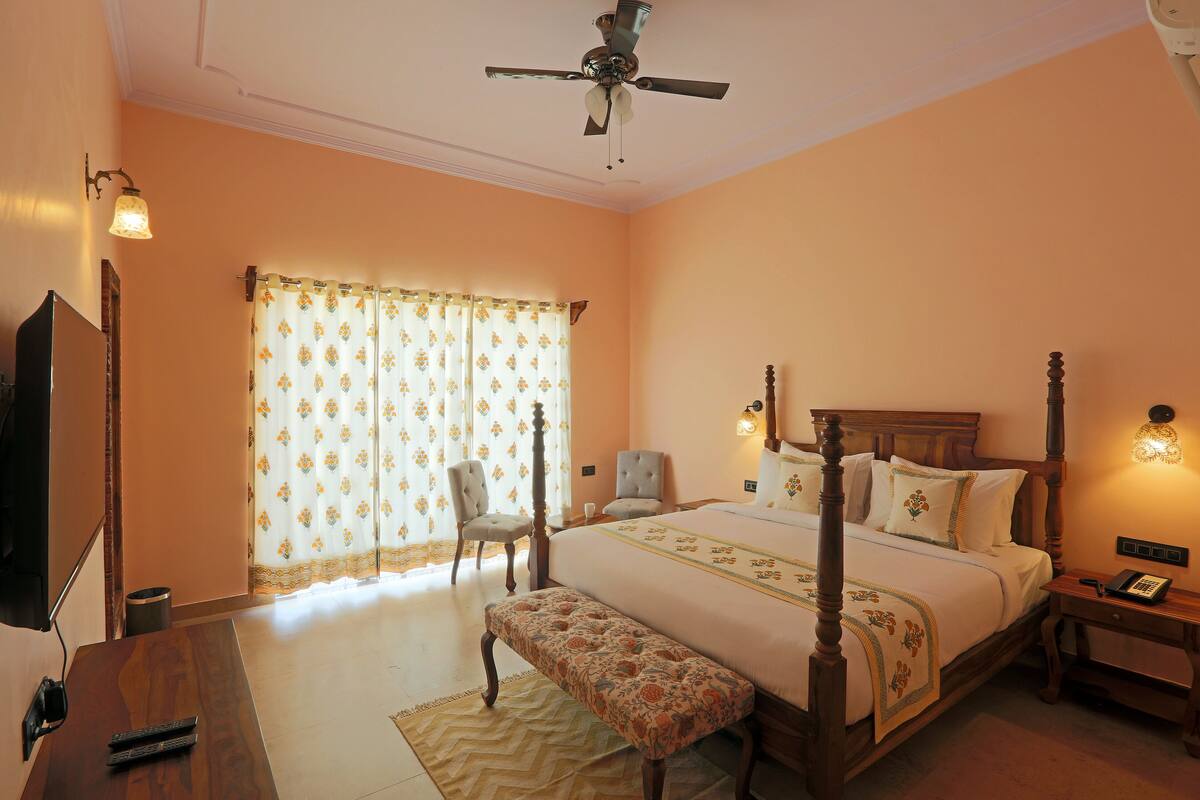 A bedroom with a four-poster bed, a bedside table with a lamp, a chair, and a television on a wooden dresser.