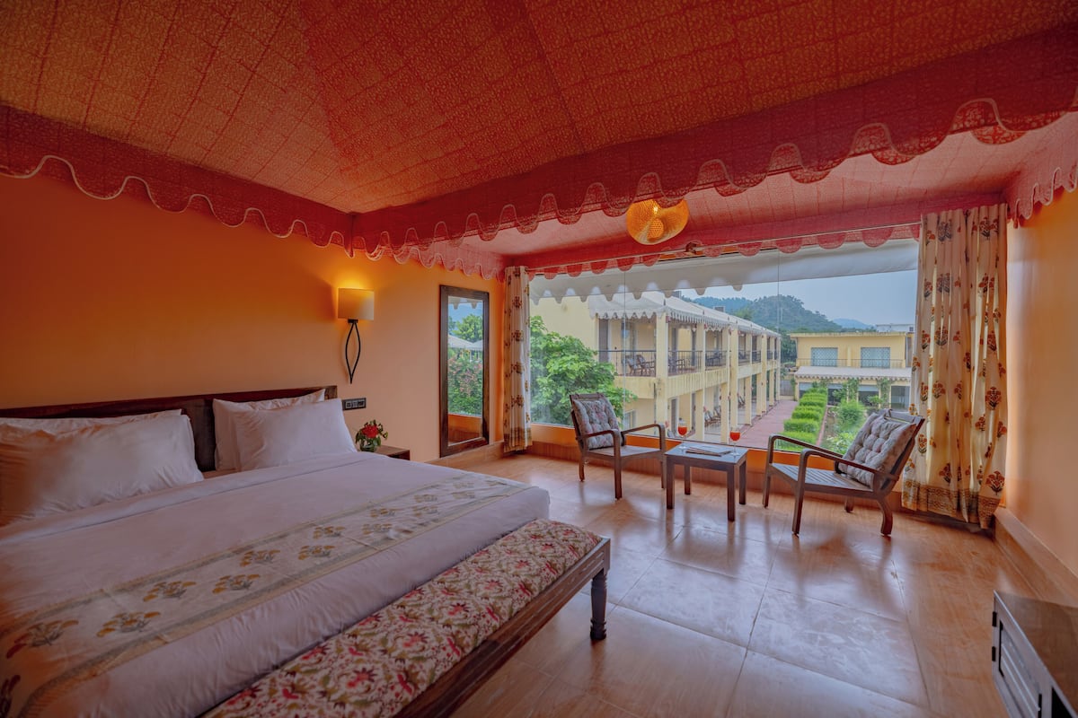 A hotel room with a large bed, a balcony with chairs, and a view of the courtyard.