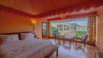 A hotel room with a large bed, a balcony with chairs, and a view of the courtyard.