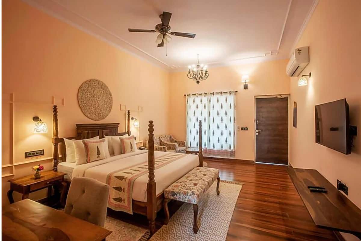 A spacious bedroom with a large bed, a ceiling fan, a chandelier, a TV, and a wooden floor.