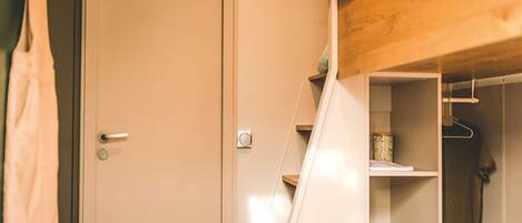 A bedroom with a wooden headboard, a closet with shelves, and a hanging garment.