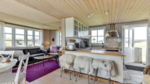 Eine moderne Küche mit Holzschnitzschränken, einer Bar mit Hockern und einem Essbereich mit einer Couch und Stühlen.