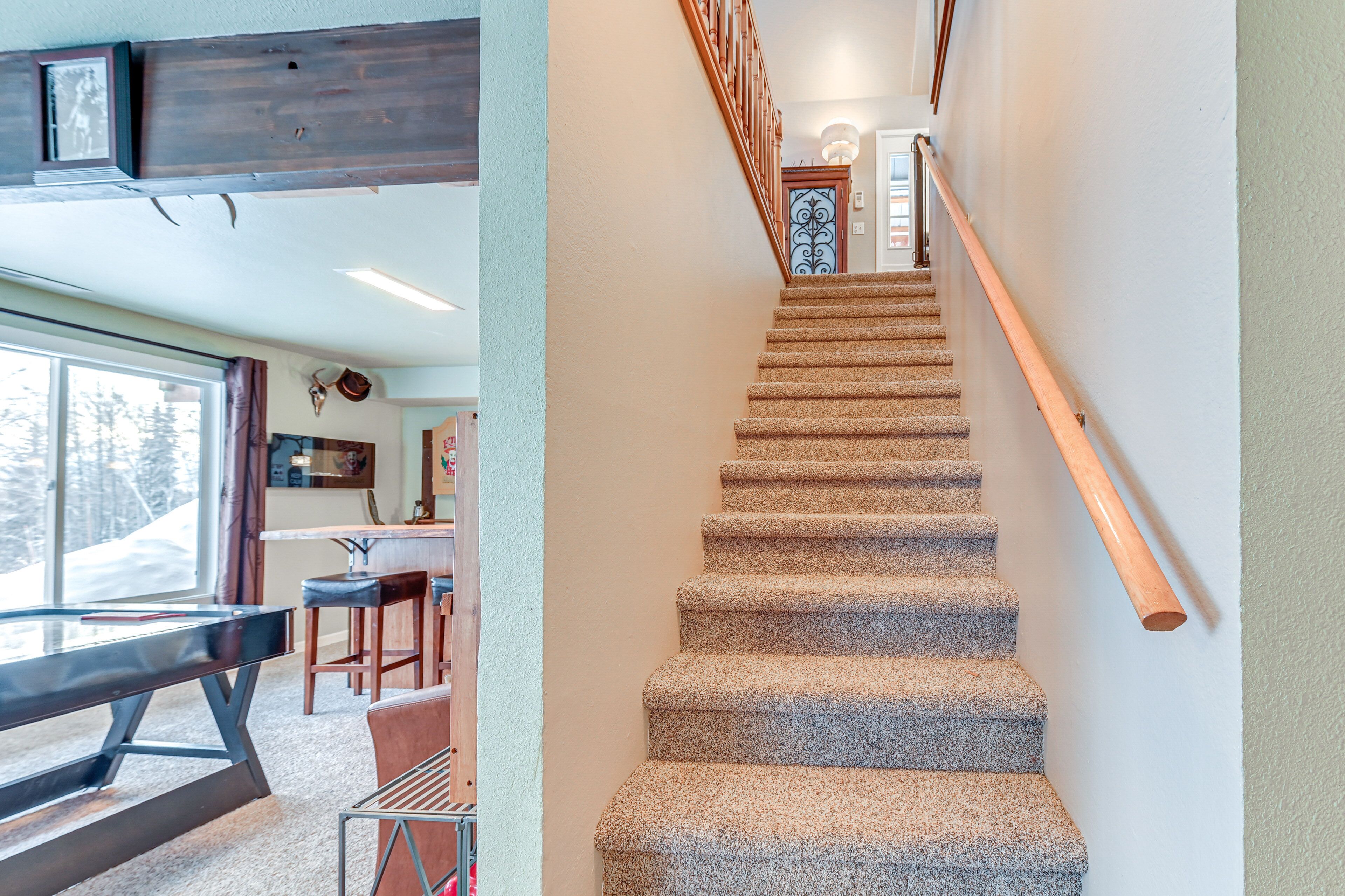 Un escalier dont les marches sont recouvertes de moquette et qui possède des rampes en bois, menant à une porte surmontée d’un portail en fer forgé décoratif.