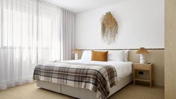A neatly arranged bedroom with a bed, bedside tables, and a wall-mounted lamp.
